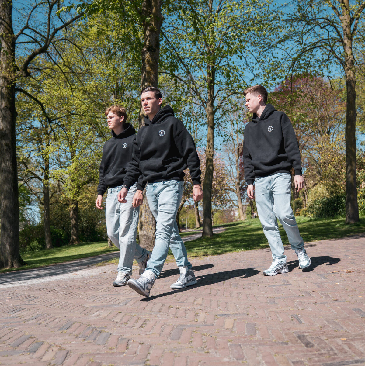 Drie mannen dragen zwarte Modern Motive streetwear outfits tijdens wandeling buiten