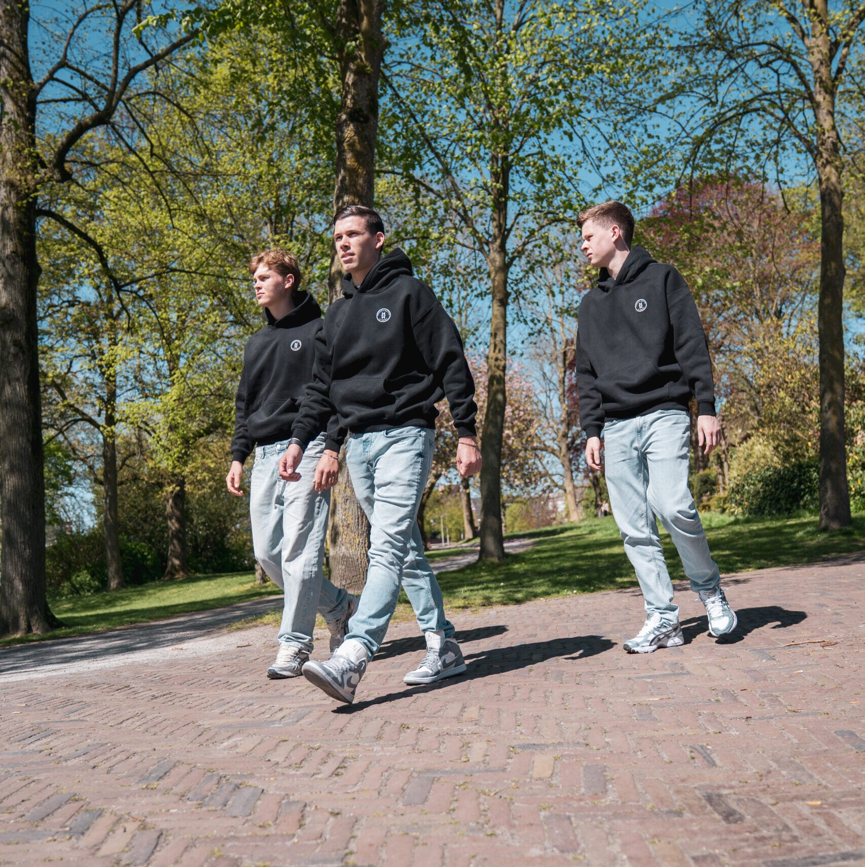 Drie mannen dragen zwarte Modern Motive streetwear outfits tijdens wandeling buiten